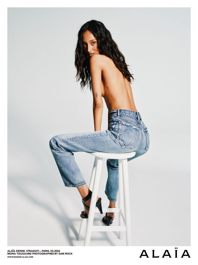 Model Mona Tougaard wearing blue denim jeans seated on a white stool against a light background for Alaïa Denim 2026