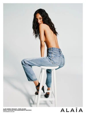 Model Mona Tougaard wearing blue denim jeans seated on a white stool against a light background for Alaïa Denim 2026