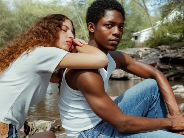A Black man and a woman with curly hair resting on his shoulder outdoors near water for Levi's Timeless campaign.