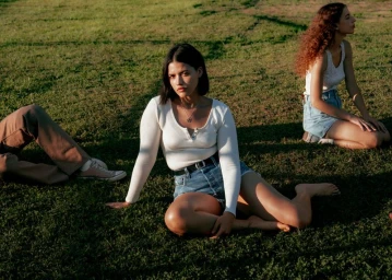 Three models relaxing on a sunny grass field wearing denim shorts and casual tops for Levi's campaign photography.