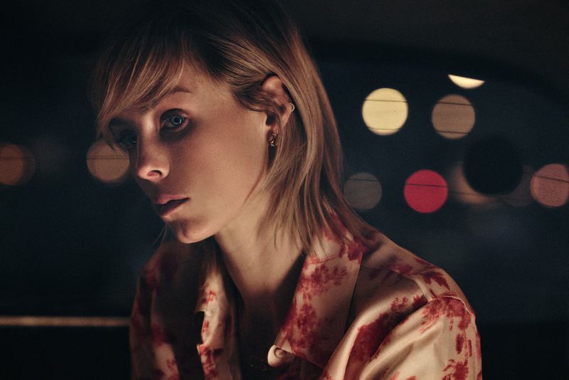 Edie Campbell in a patterned red and white blouse against a dark background with blurred lights for Carolina Herrera