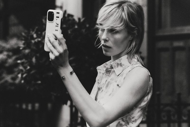 Edie Campbell taking a selfie with a smartphone for Carolina Herrera Matryoshka Pocket project, shot in black and white.