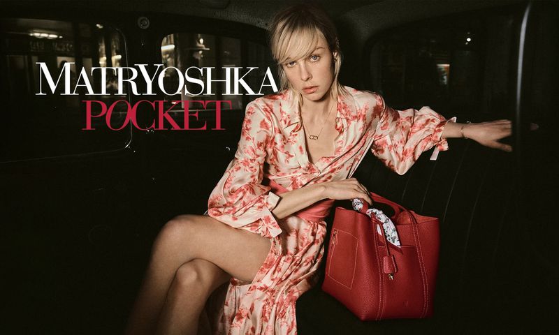 Elegant adult female in a patterned kimono poses with a red leather handbag inside a car for a fashion campaign.