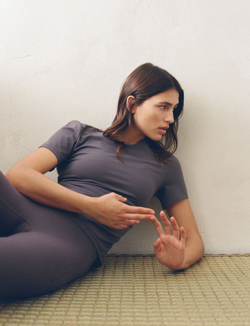 Model in grey activewear t-shirt and leggings resting on a woven mat against a pale wall for H&M Move Cotton Active