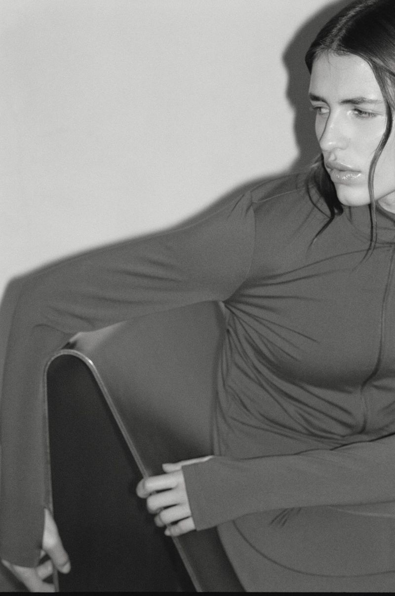 Monochrome portrait of a woman wearing an activewear top posing indoors against a plain wall.