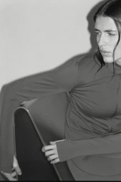Monochrome portrait of a woman wearing an activewear top posing indoors against a plain wall.