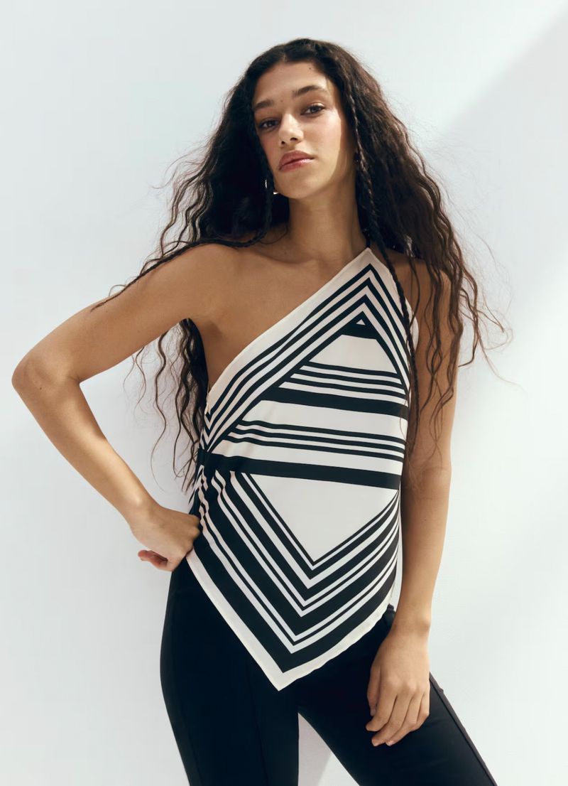 Model with long dark wavy hair wearing a geometric black and white patterned top against a plain white background.