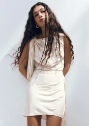Model with long dark braided hair wearing a cream dress against a bright white background