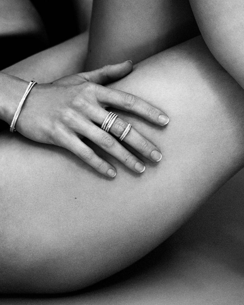 Close-up monochrome image of a hand wearing diamond rings and a bracelet resting on a leg for Repossi