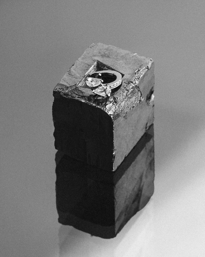 Diamond ring resting on top of a dark textured stone block against a neutral background.