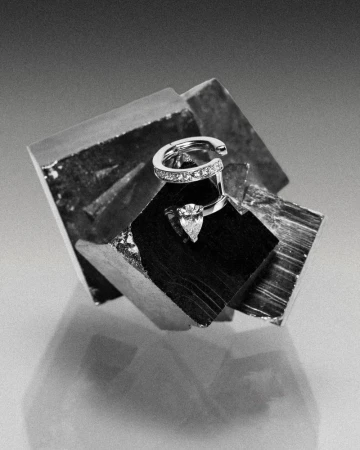 Repossi diamond ring resting on a faceted metallic mineral crystal under monochrome studio lighting.