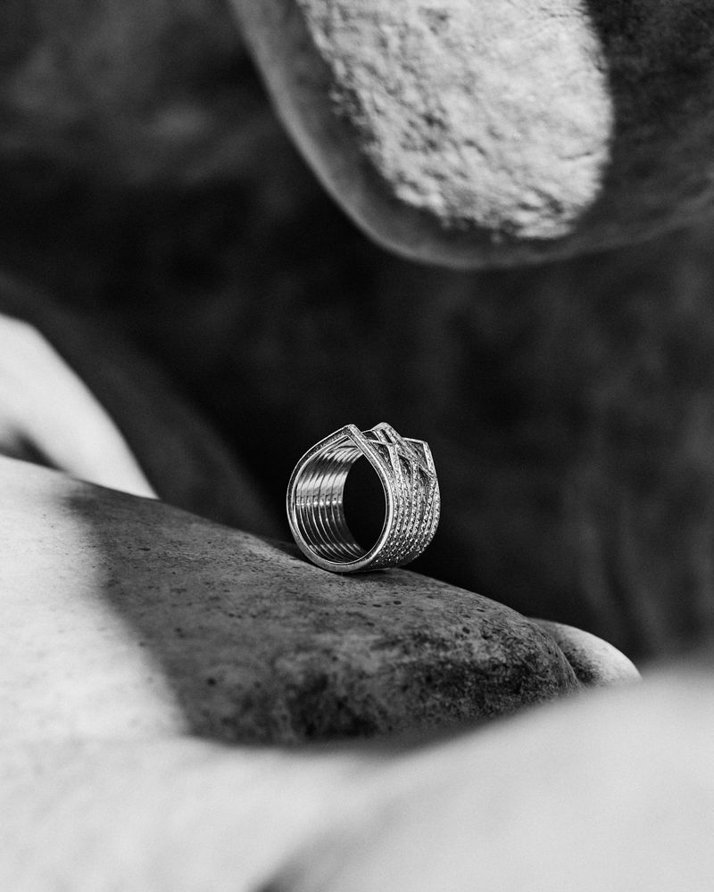 Close-up monochrome product shot of a Repossi ring resting on a textured stone surface with natural shadows.