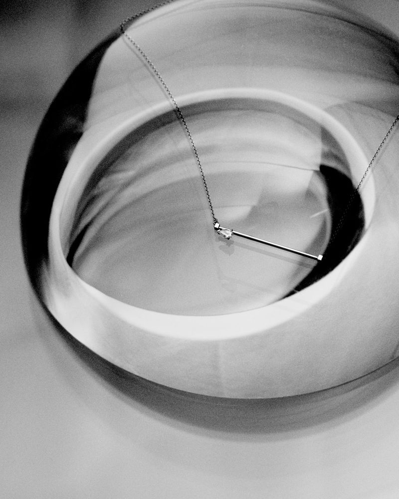 Close-up product shot of a silver diamond pendant necklace resting inside a curved reflective glass object.