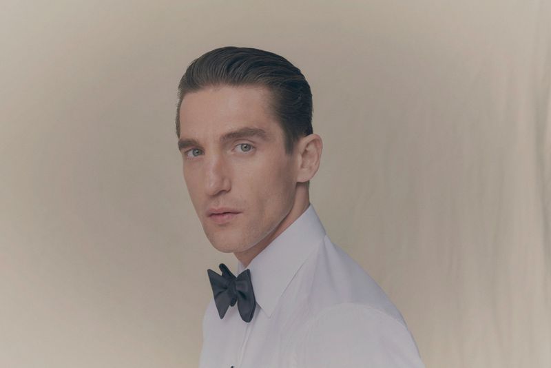 Portrait of a man wearing a white dress shirt and a black bow tie against a seamless neutral backdrop.