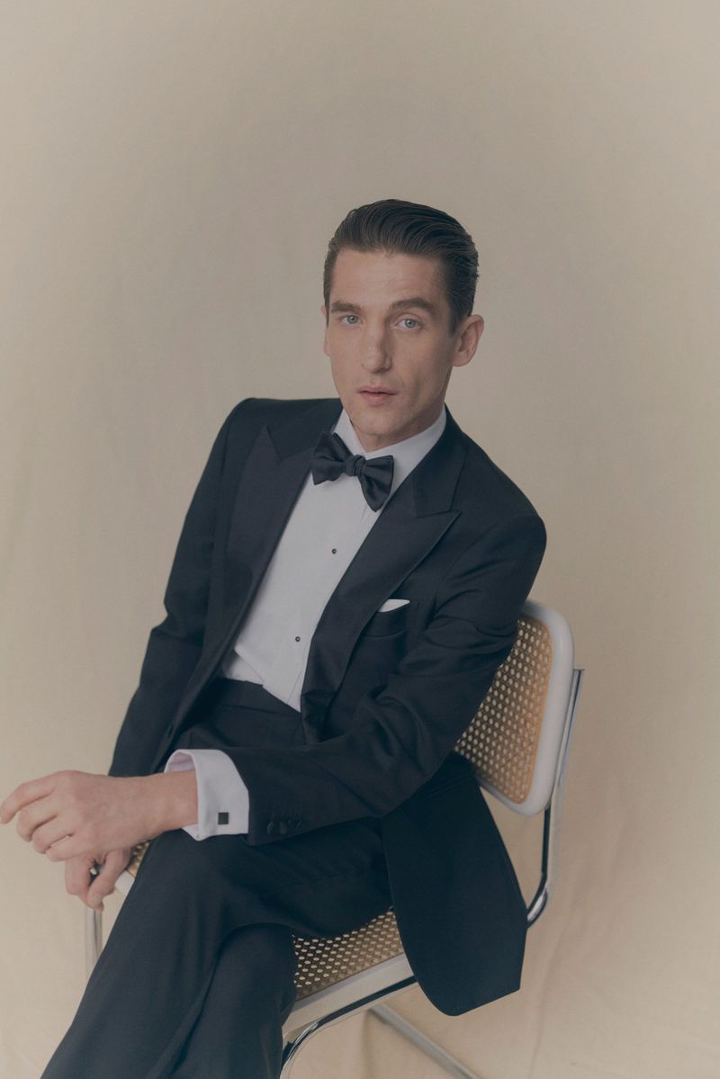 Man wearing a black tuxedo and bow tie seated on a chair against a neutral background for Eton of Sweden