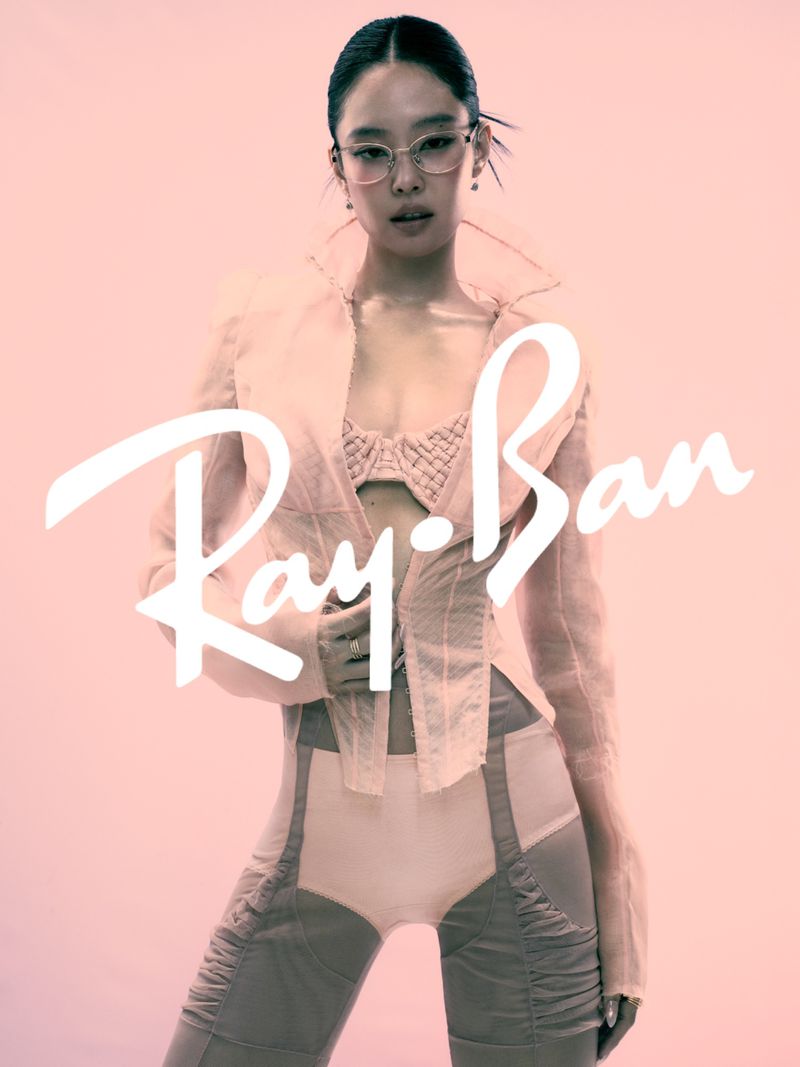 Jennie wearing clear-framed glasses and a light jacket against a pink backdrop with Ray-Ban logo overlay