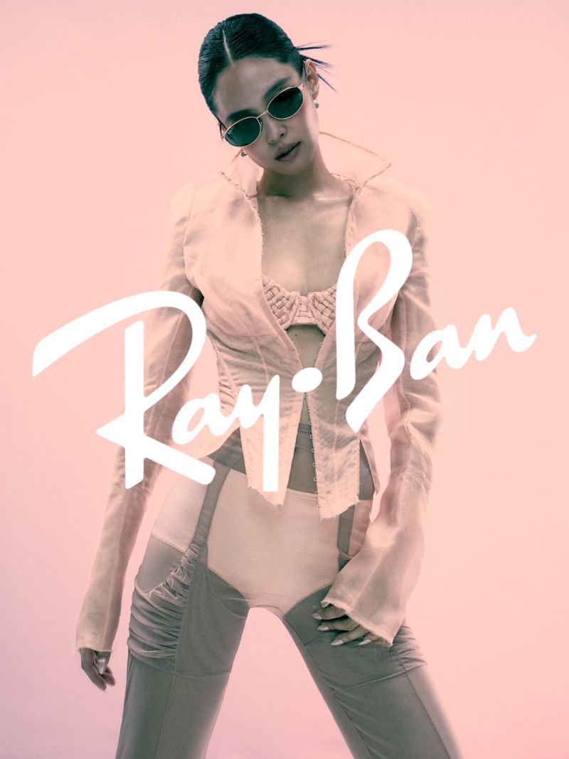 Jennie wearing dark sunglasses and a sheer pink jacket against a soft pink background for Ray-Ban