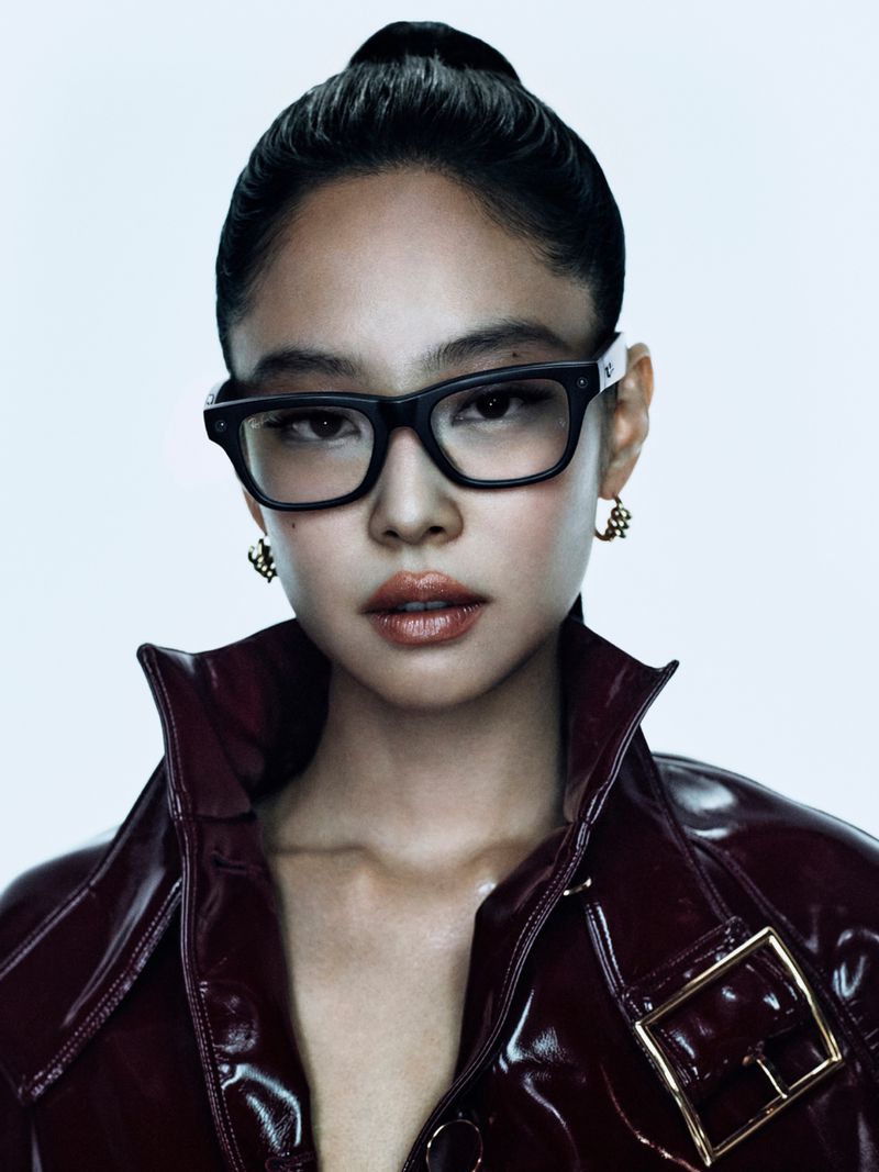 Jennie wearing black Ray-Ban glasses and a glossy burgundy jacket against a white background