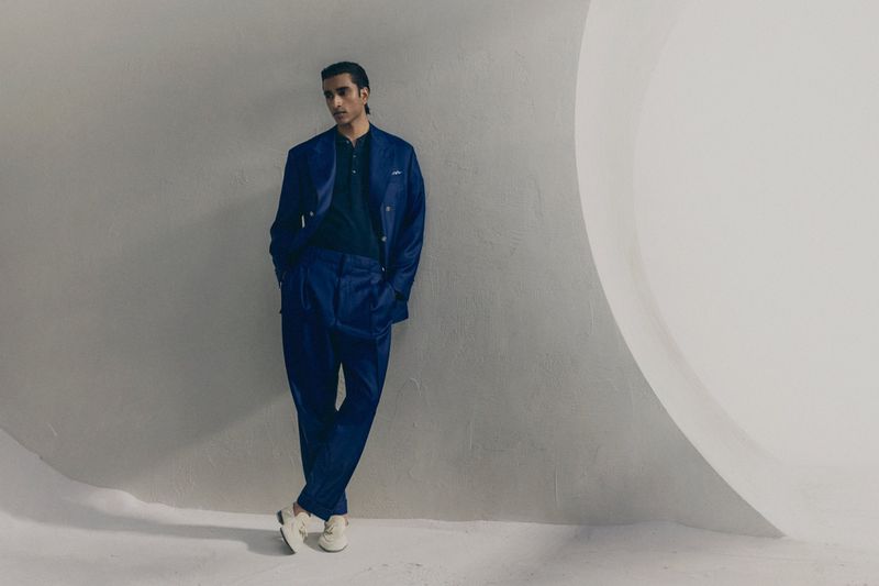 Jeenu Mahadevan in a blue suit leaning against a curved white wall for Brunello Cucinelli