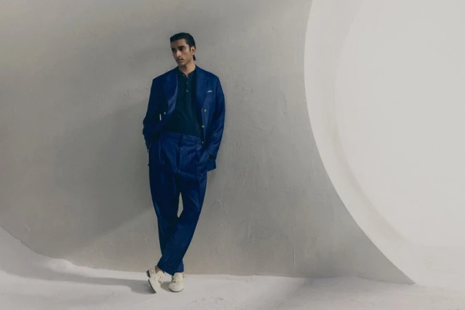 Jeenu Mahadevan in a blue suit leaning against a curved white wall for Brunello Cucinelli