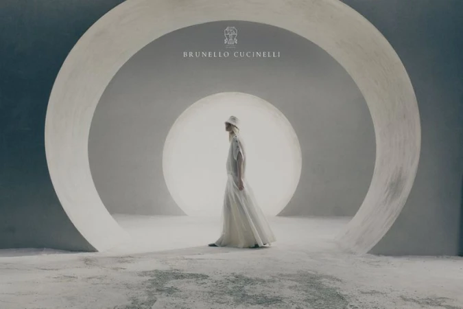 Model wearing a light flowing skirt and hat walking through large minimalist concrete circular arches