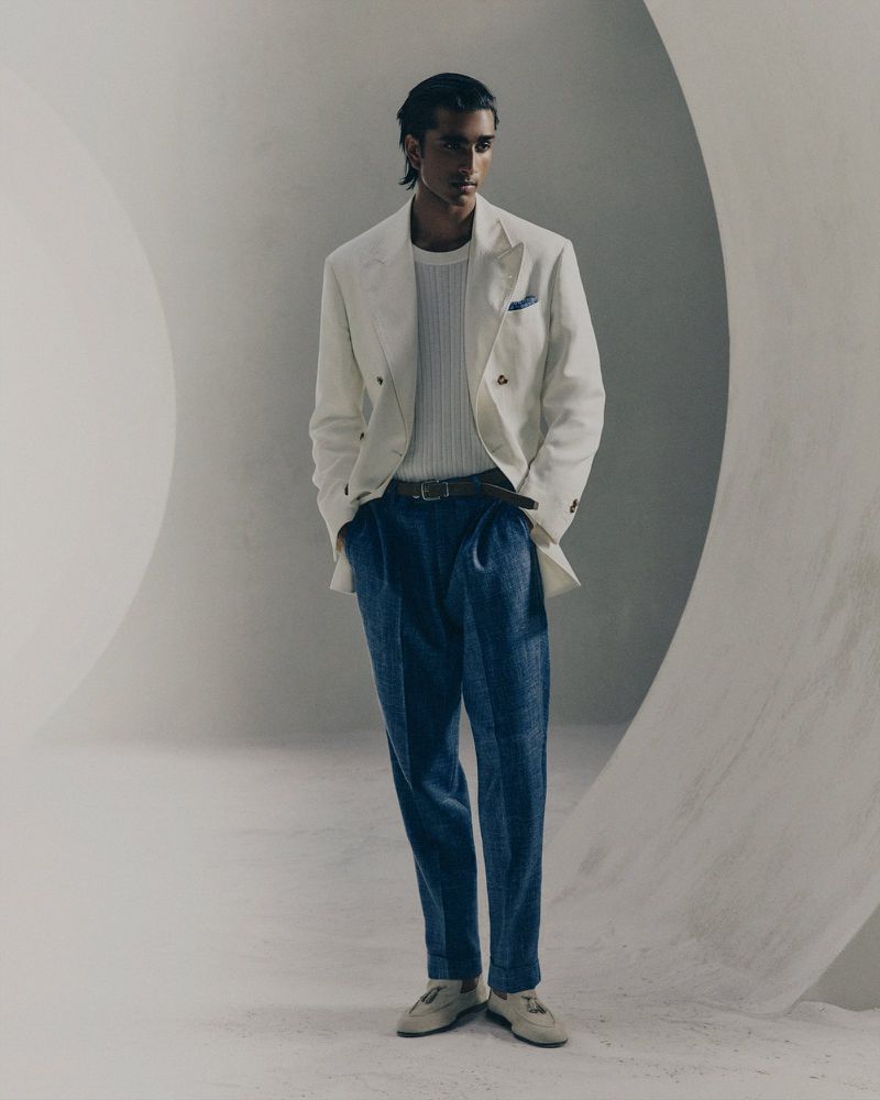 Model wearing a white double-breasted blazer and blue trousers in a minimalist architectural studio set