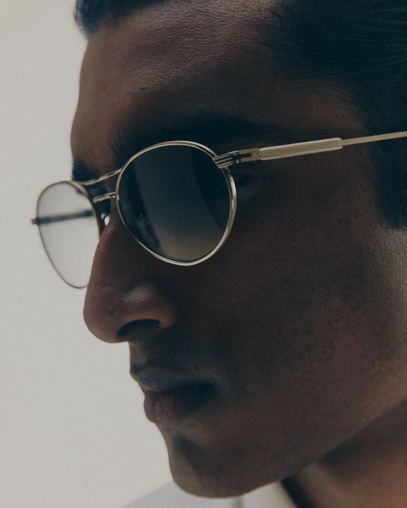Close-up portrait of a man wearing metal-frame sunglasses against a white background