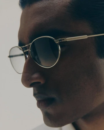 Close-up portrait of a man wearing metal-frame sunglasses against a white background