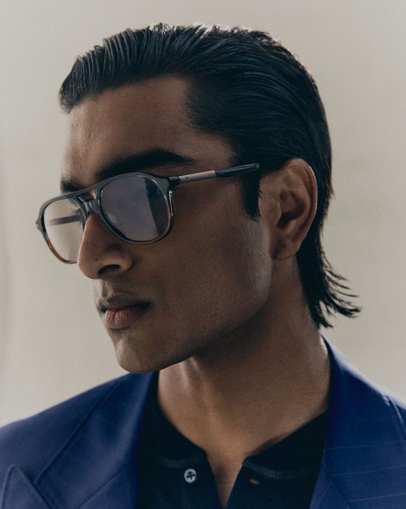 Close-up portrait of a South Asian male model wearing tinted aviator glasses and a blue blazer for Brunello Cucinelli.