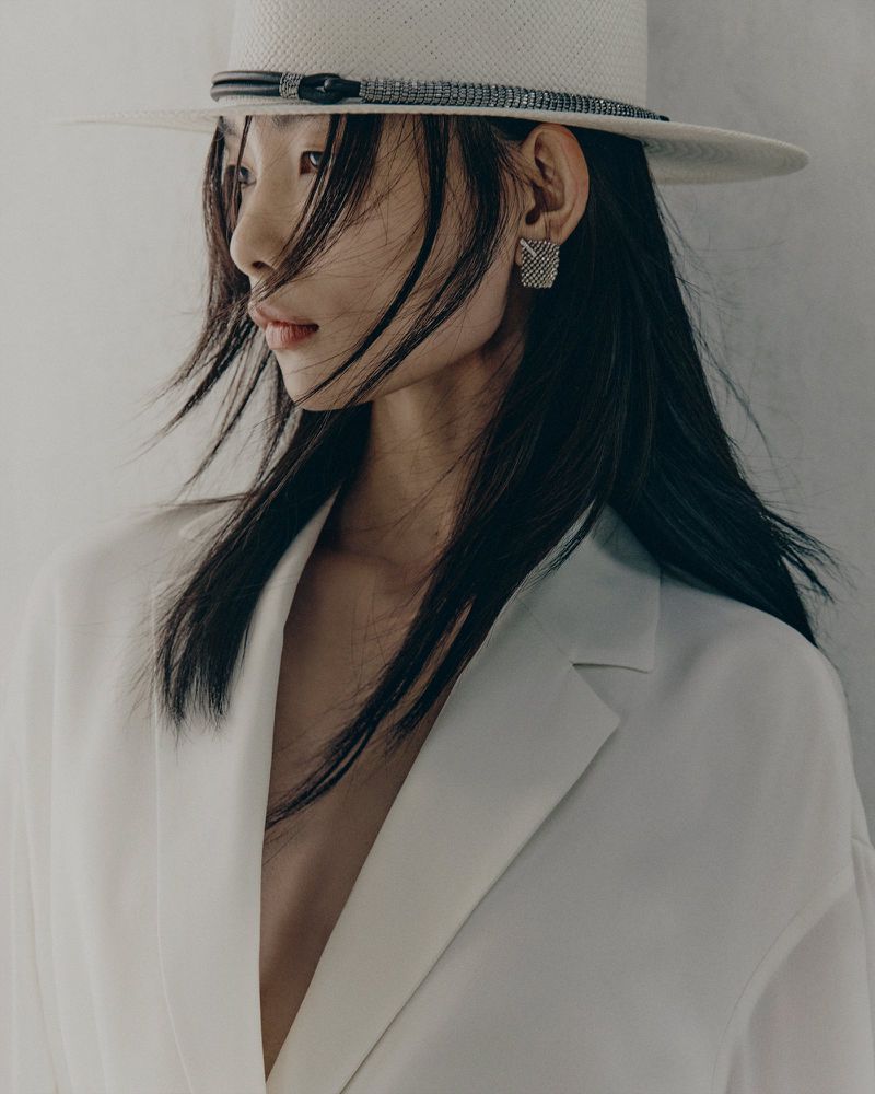 Model wearing a white fedora hat and white blazer against a neutral backdrop