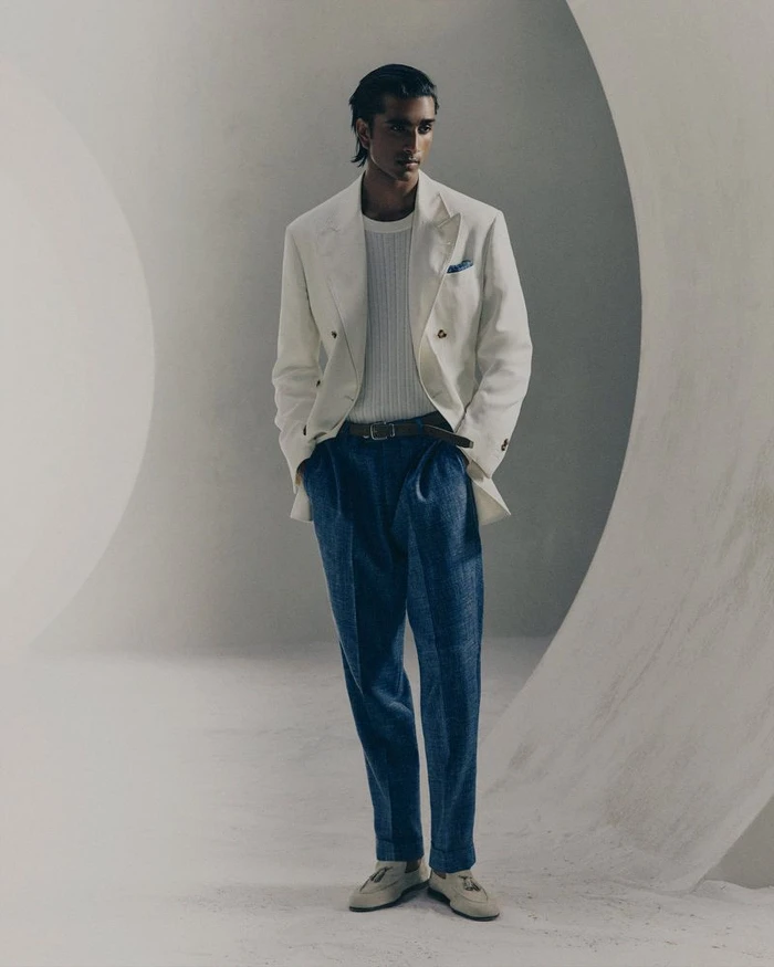 Model wearing a white double-breasted blazer and blue trousers in a minimalist architectural studio set