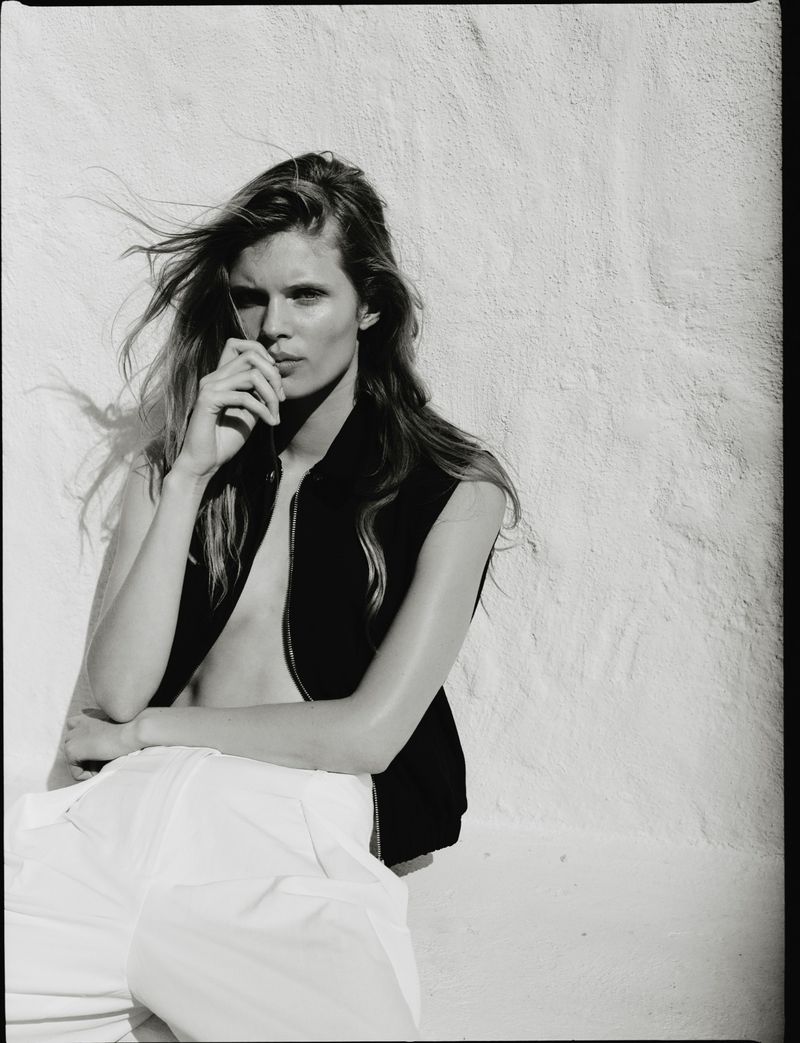 Model Ida Heiner wearing a black vest and white trousers against a white textured wall for Zara