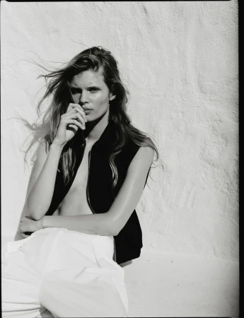 Model Ida Heiner wearing a black vest and white trousers against a white textured wall for Zara