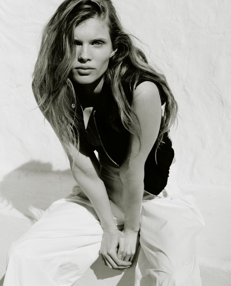Model Ida Heiner wearing a black top and white trousers against a bright textured wall for Zara March 2026.