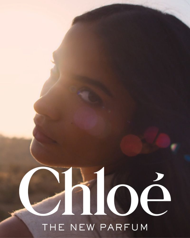 Close-up portrait of a young adult woman with dark hair, in profile, with blurred background and Chloe brand logo, 'The New Parfum' text.