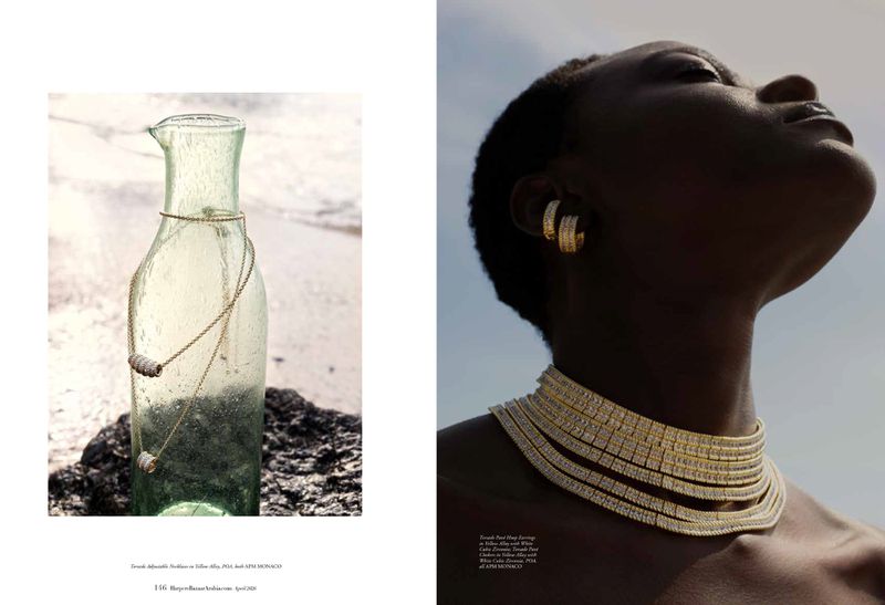 Black woman wearing gold hoop earrings and layered diamond necklaces with glass bottle on rock by water
