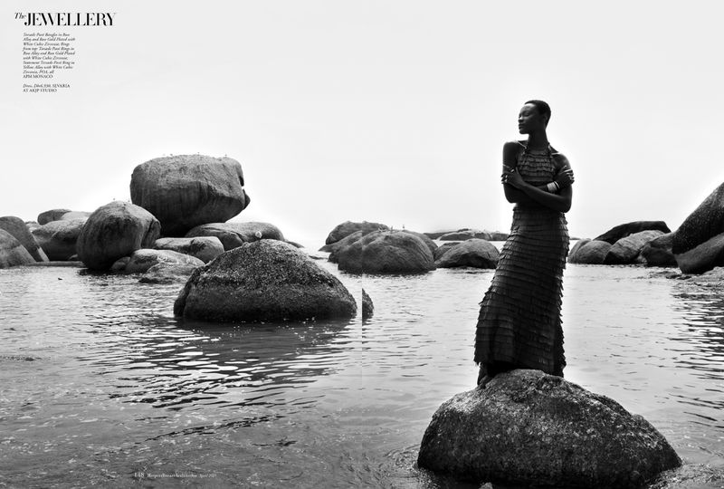 Black model standing on a coastal boulder in water surrounded by rocky outcrops for Harper's Bazaar Arabia editorial