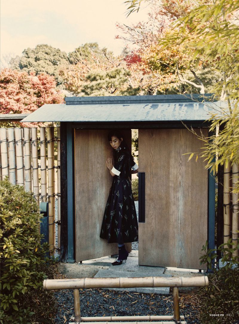 Model stepping through wooden double doors surrounded by a bamboo fence and trees for Vogue Philippines Zen Life.