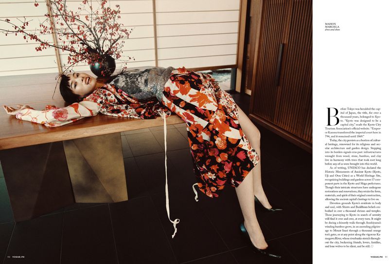 Asian woman lies on a table in a floral kimono with an Ikebana flower arrangement, shot indoors with dark floors and natural light.