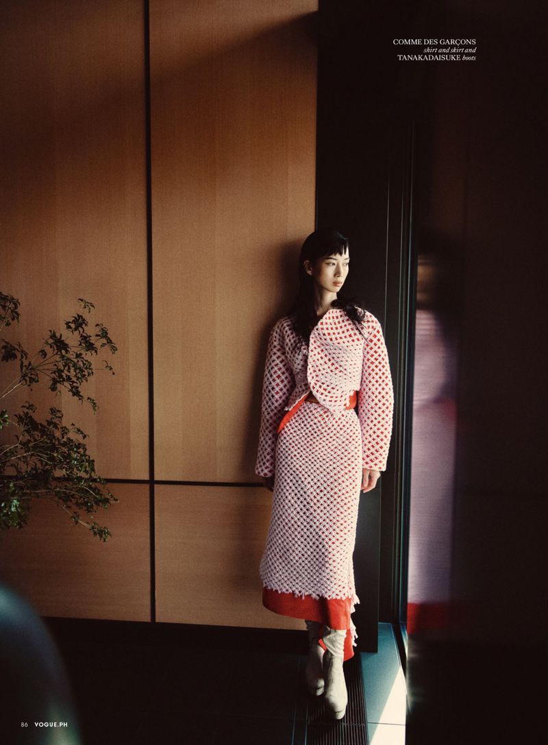 Model wearing a patterned textured skirt and jacket standing against a wooden wall interior