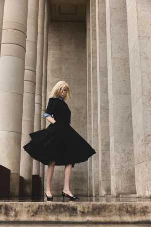 Model in a black flared dress and heels standing amid massive stone columns for Numero Netherlands editorial.