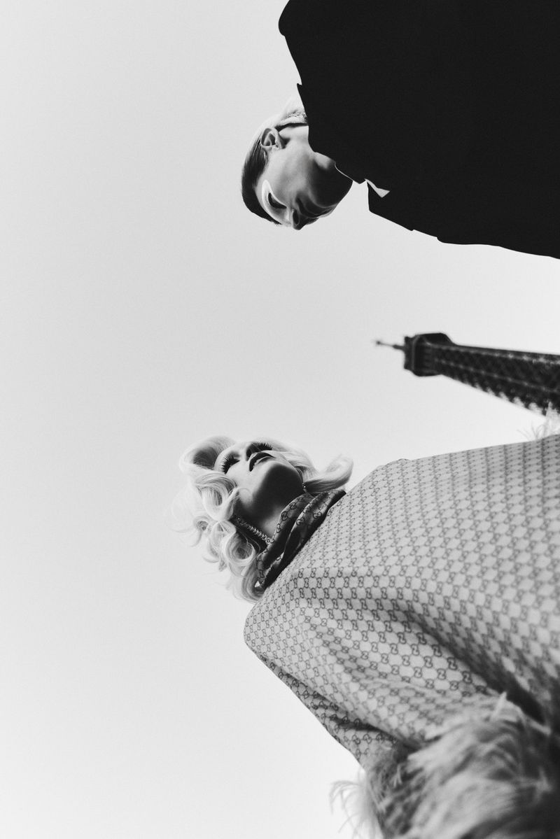 Low-angle black and white fashion editorial photograph featuring two models outdoors with the Eiffel Tower visible in the background.