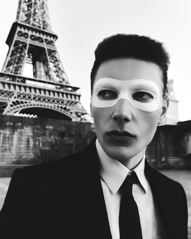 Monochrome portrait of a man wearing a white eye mask and a suit with the Eiffel Tower in the background for Numero Netherlands.