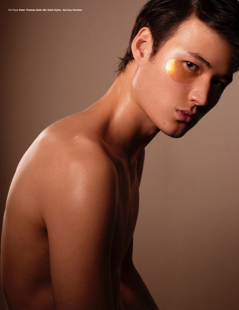 Close-up portrait of a shirtless young man with an eye mask, against a neutral backdrop, showcasing beauty and skincare.