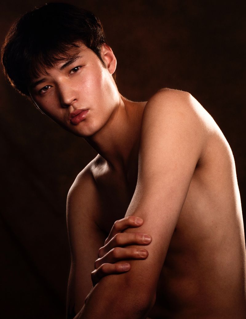Shirtless young man posing with arms crossed against a dark textured studio background in a portrait photograph by B Charles Johnson.