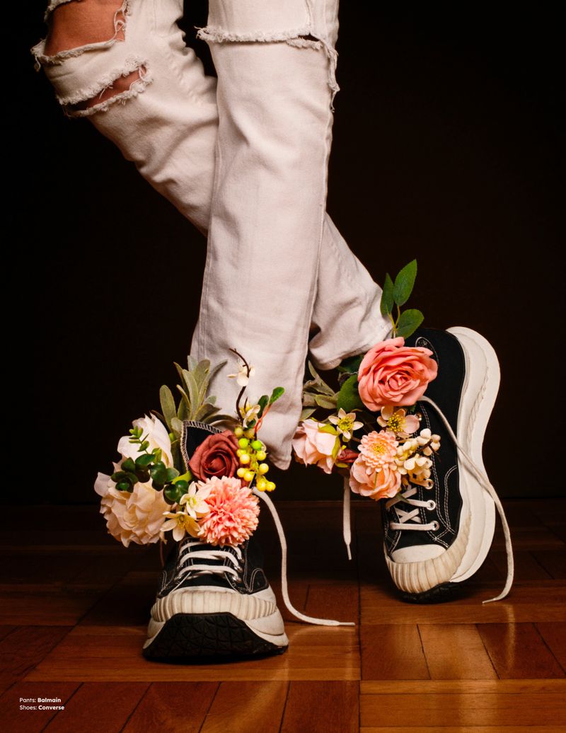 Close-up of crossed legs wearing distressed white jeans and platform sneakers overflowing with floral arrangements