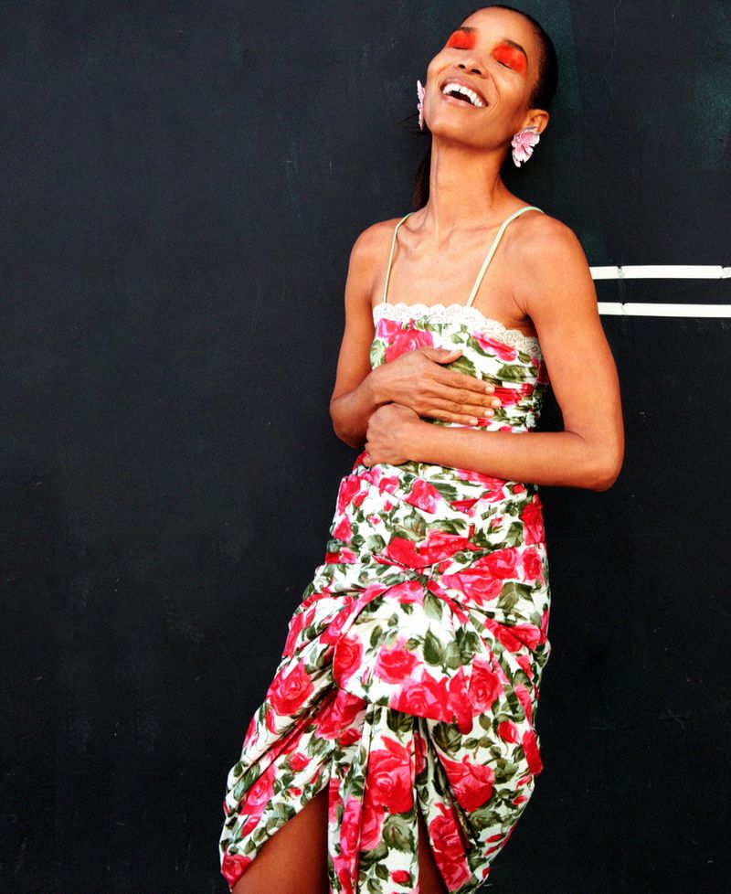 Model in a floral print dress with vibrant red eye makeup leaning against a dark wall for M Le magazine du Monde