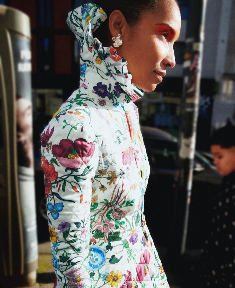 Profile of a model wearing a high-collared floral patterned quilted jacket outdoors on a city street.