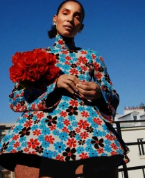 Model in a floral patterned dress holding a bouquet of red roses against a clear blue sky background