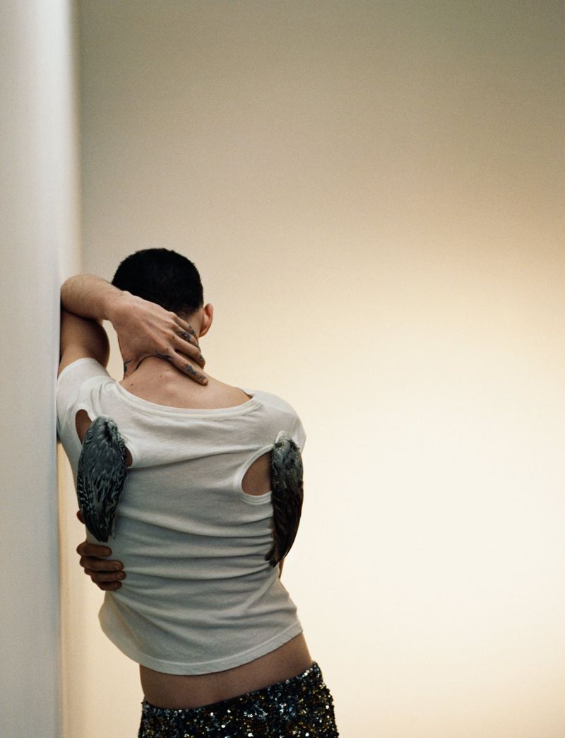 Adult poses with peregrine falcons perched on a white t-shirt against a gradient white and beige background in a studio fashion shot.